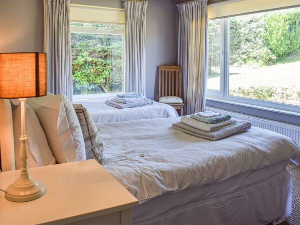 "Bright and airy bedroom with twin beds, wooden furniture, and coastal decor."