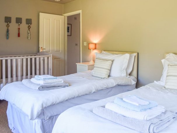 "Bright and airy bedroom with twin beds, wooden furniture, and coastal decor."